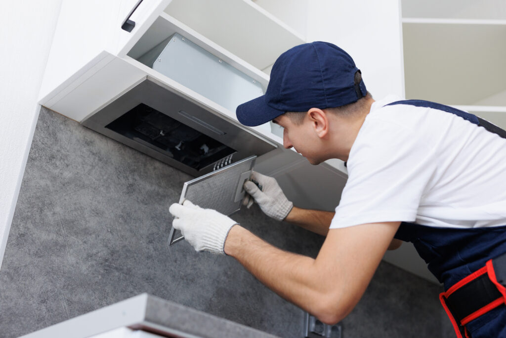 Mans hands removing a filter from cooker hood for cleaning. Replacing filter in kitchen hood.